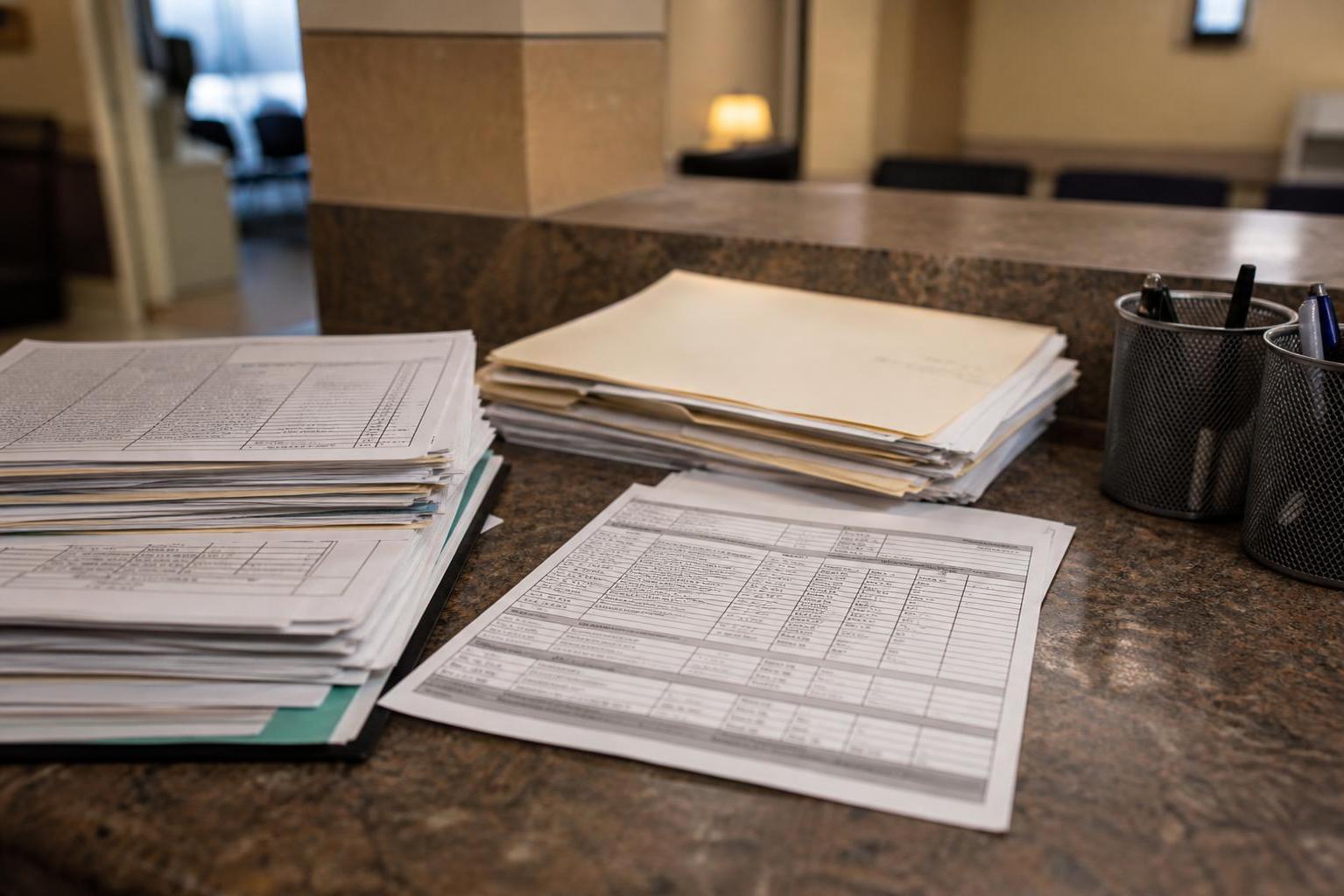 Stacks of forms and folders sit on a reception counter with pen holders
