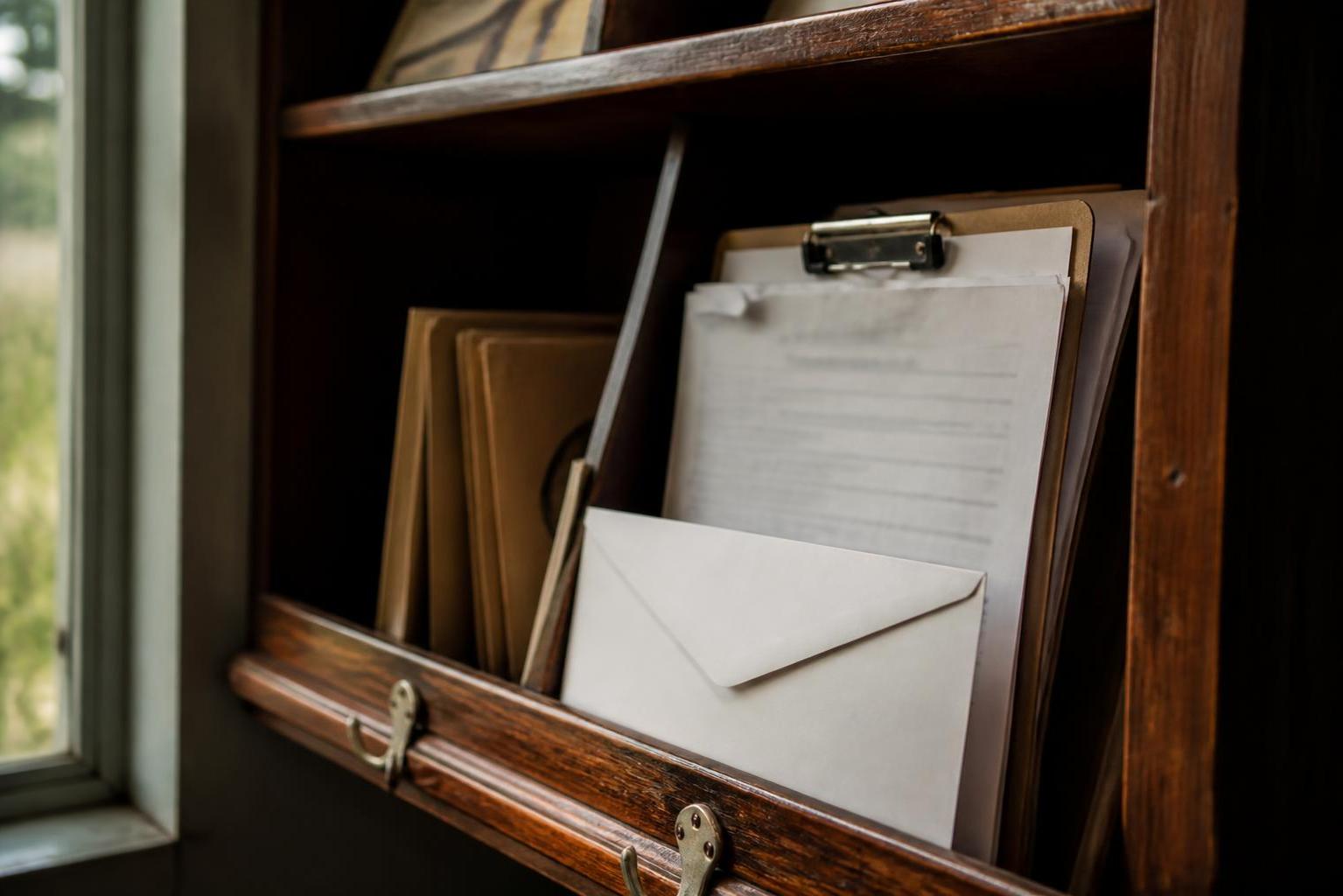 A wooden mail organizer holds envelopes, folders, and a clipped document beside a window