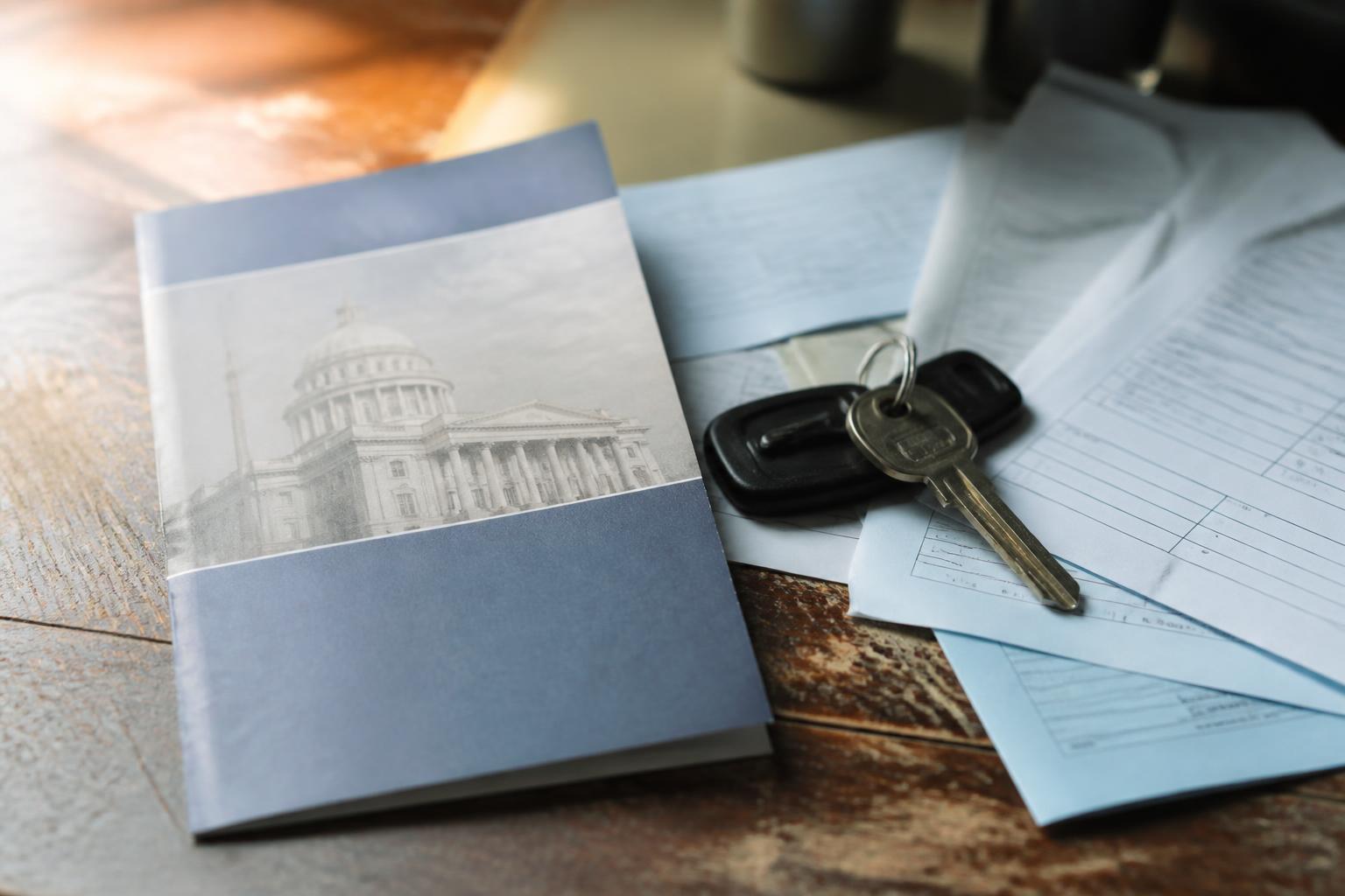 Keys, blue forms, and a booklet rest on a wooden table