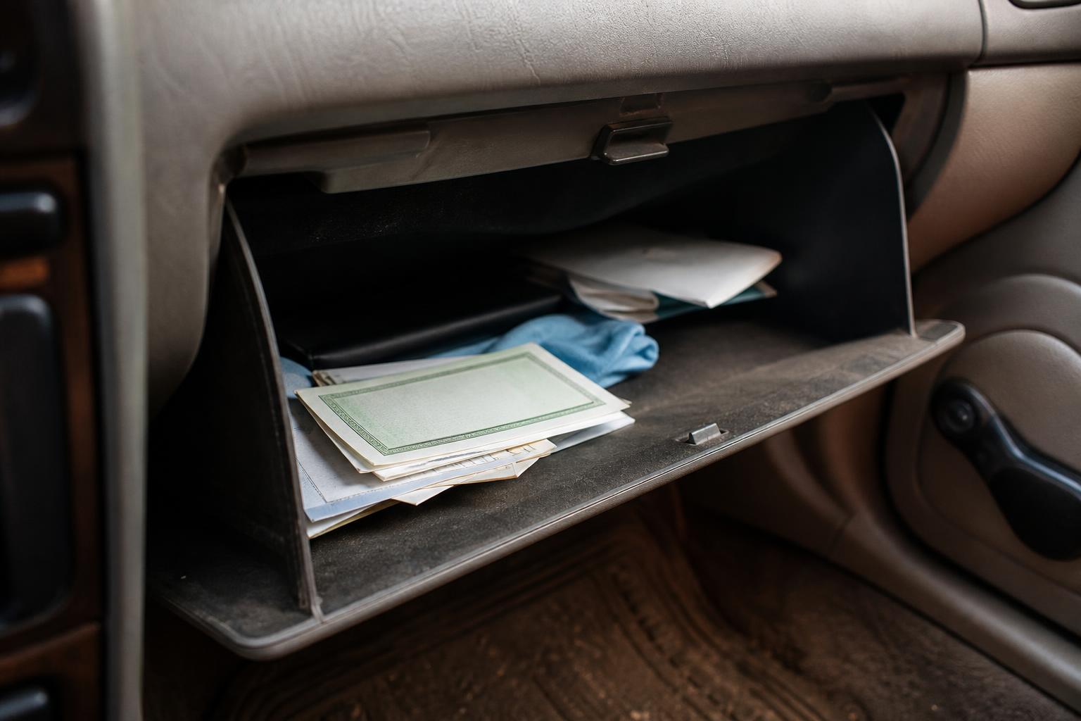 An open car glove compartment contains papers, folders, and a blue cloth