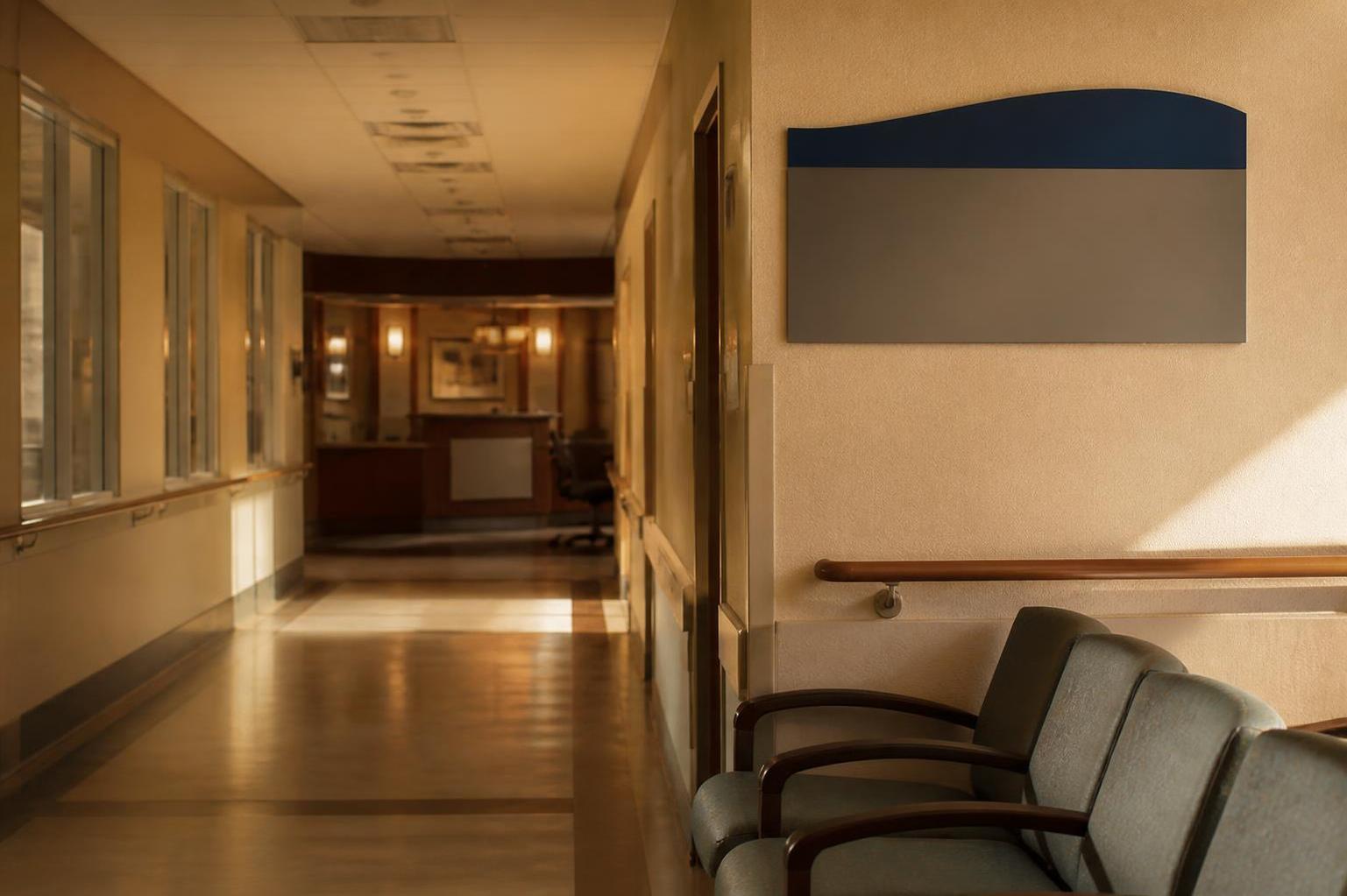 Hospital hallway contains chairs, wall sign, handrail, windows, and reception desk