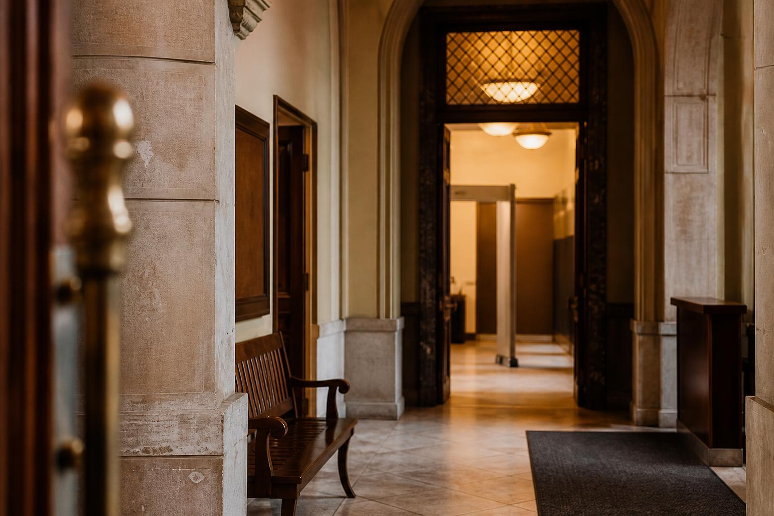 A hallway with arched doorways, benches, columns, and ceiling lights is visible