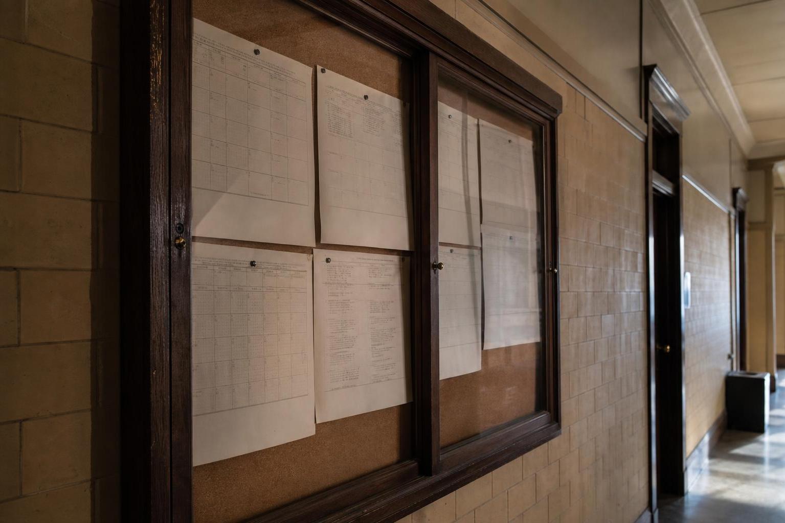 Pinned papers hang inside glass-front bulletin boards along a tiled hallway